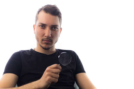 Handsome young man with magnifier, selective focus on eyes. Portrait on a white background.の写真素材