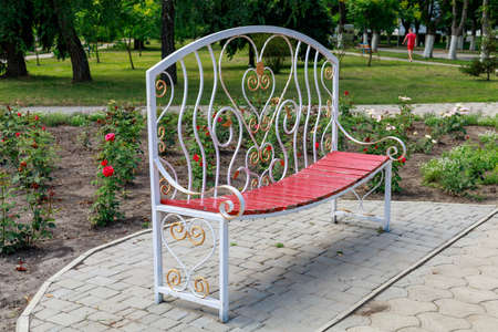 A very beautiful bench for lovers in a city park with flower beds and flowers. Heart as a symbol of love. Selective focus background, copy space for text or letteringの写真素材