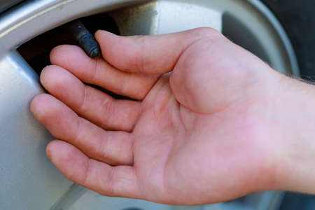 The hand twists or unscrews the nipple cap from the car wheel. Place the air replenishment tires....