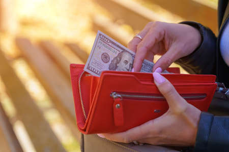 A womans hand pulls a hundred dollar bill out of her wallet. Background with copy space for text or inscriptions.の写真素材