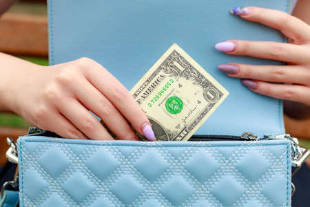 A womans hand takes a dollar out of her wallet. Background with copy space for text or inscriptions.