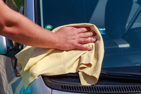 A hand with a dry rag wipes the windshield of a car at a car wash. Background with copy space for text or lettering. Illustrative editorial. July 23, 2021, Balti Moldova.のeditorial素材