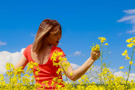 Young pretty woman in colored dress on lightning cheerful yellow background of blooming rapeseed...