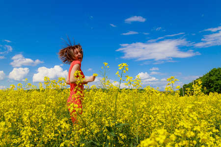 Young pretty woman in colored dress on lightning cheerful yellow background of blooming rapeseed field. Inspiration conceptの写真素材