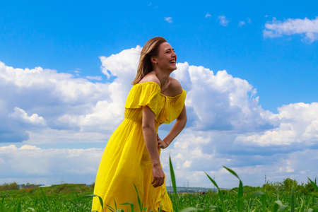 Young woman in a yellow dress outdoors in a green field. Good laughing mood.の写真素材