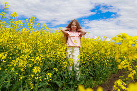 Childhood happiness concept. Teenager straightens hair outdoors. Girl in nature, lifestyle. Cheerful lightning yellow color of blooming rapeseed field on the background.の写真素材