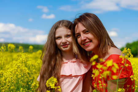 Mom and daughter in nature outdoors lifestyle. Cheerful lightning yellow color of blooming rapeseed field on the background. Portrait of smiling peopleの写真素材
