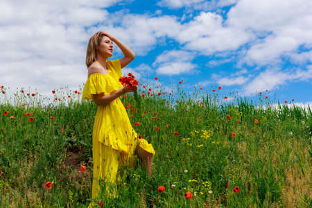 Cute young woman in yellow dress enjoys a stroll through the poppy field. Outdoor, lifestyleの写真素材