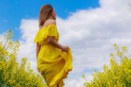 Young pretty woman in yellow dress on lightning cheerful yellow background of blooming rapeseed field. Good mood conceptの写真素材