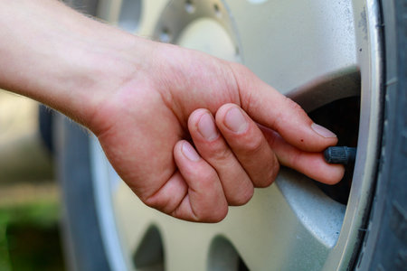 The hand twists or unscrews the nipple cap from the car wheel. Place the air replenishment tires. Toned background with copy space for text or lettering.の写真素材