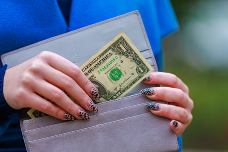 A womans hand pulls a hundred dollar bill out of her wallet. Background with copy space for text or inscriptions.の写真素材