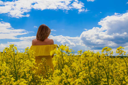 Young pretty woman in yellow dress on lightning cheerful yellow background of blooming rapeseed field. Pleasure conceptの写真素材