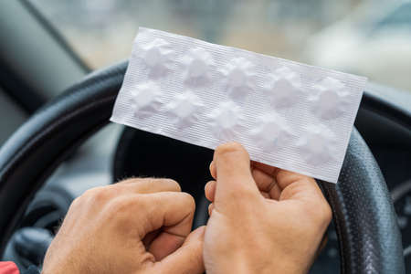 Pack of pills in the hands of the driver on a blurred background of the steering wheel in the car....
