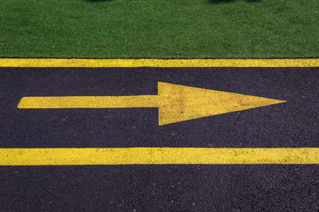 Yellow arrow to the right on the black asphalt of the bike path in the park. Background with copy...