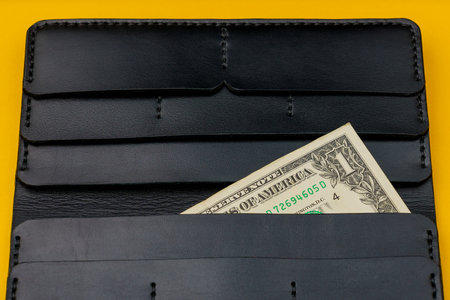 Corner of a cash 1 dollar bill with a leather wallet in the background. Selective focus, copy space for textの写真素材