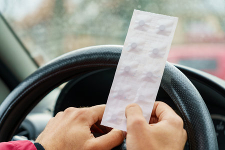 Pack of pills in the hands of the driver on a blurred background of the steering wheel in the car. The use of pharmacological drugs for medical purposes while driving. Selective focusの写真素材