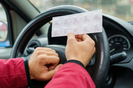 Pack of pills in the hands of the driver on a blurred background of the steering wheel in the car. The use of pharmacological drugs for medical purposes while driving. Selective focusの写真素材