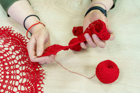 Hands of a craftswoman with a ball of red threads. Unusual hobby crochet. Background with copy space...