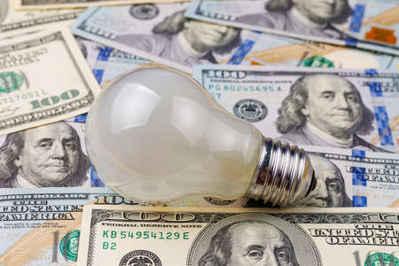 Classic electric light bulb on a blurred background of dollar cash bills or banknotes. The concept of the energy crisis and electricity inflation. Rise in electricity prices. Copy space for text.の写真素材