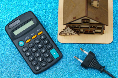 Plug from an extension cord on a blurred background of a calculator and symbolic house, selective focus. The concept of the energy crisis and electricity inflation. Rising electricity pricesの写真素材