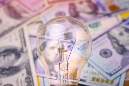 Classic electric light bulb on a blurred background of dollar cash bills or banknotes. The concept...