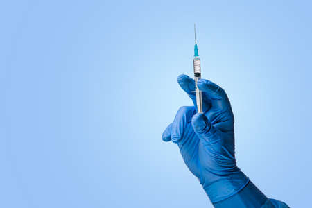 Doctors hand in surgical gloves holds a syringe on a classic symbolic blue backgroundの写真素材