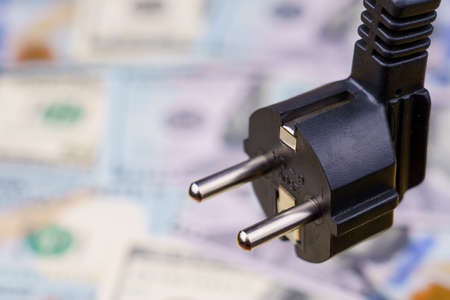 Electric cord plug and dollars on a blurred background, selective focus. The concept of the energy...