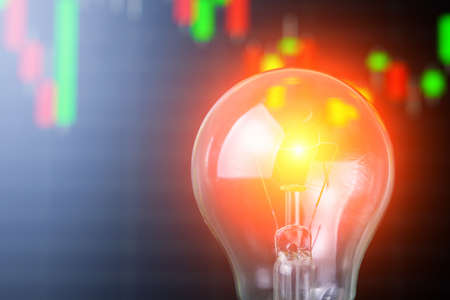 Classic incandescent light bulb on blurred background of abstract toned stock chart, selective focus. The concept of the energy crisis and electricity inflation. Rising electricity pricesの写真素材