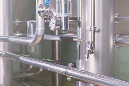 Beer tap in a brewery with industrial stainless steel pipes on a blurred background