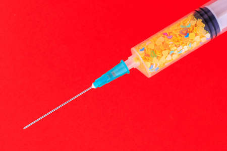 A classic disposable syringe filled with symbolic hearts. Love concept. Background with copy space for text. Red backdrop.の写真素材