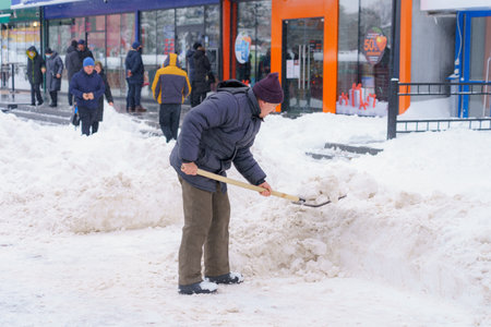 A man with a shovel removes snow in the city. Snowy cold winter. December 28, 2021 Balti Moldova.のeditorial素材