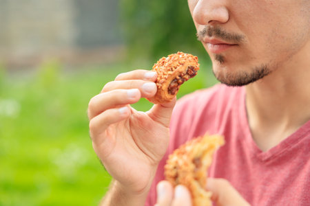 Chewing his mouth while eating, the guy eats sweet pastries with jam. Background with selective focus and copy space for textの写真素材