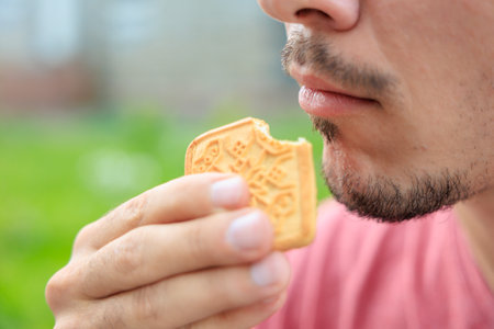 Chewing mouth while eating, guy eats square cookies. Background with selective focus and copy space for textの写真素材