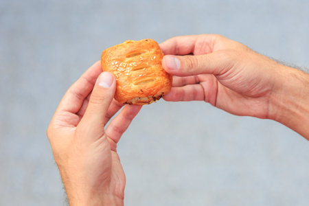 A guy's hand holds a mini puff pastry with cheese, snack and fast food concept. Selective focus on hands with blurred background and copy space for text.の写真素材