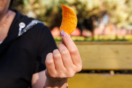 Woman's hand holding chips, snack and fast food concept. Selective focus on hands with blurred background and copy space for text.の写真素材