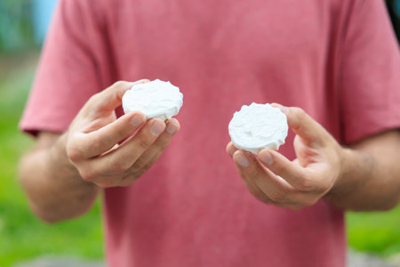 Guy's hand holds marshmallow, snack and fast food concept. Selective focus on hands with blurred background and copy space for text.の写真素材