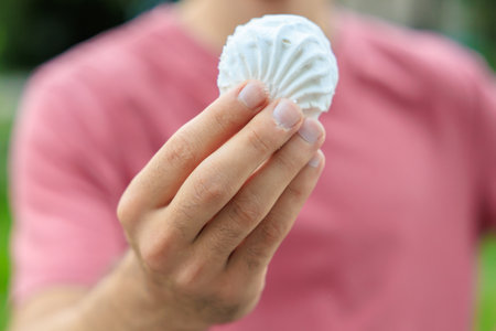 Guy's hand holds marshmallow, snack and fast food concept. Selective focus on hands with blurred background and copy space for text.の写真素材