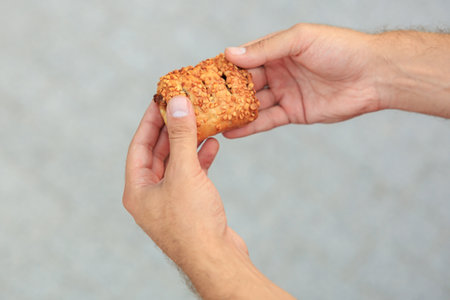 A guy's hand holds a sweet pastry with jam, snack and fast food concept. Selective focus on hands with blurred background and copy space for text.の写真素材
