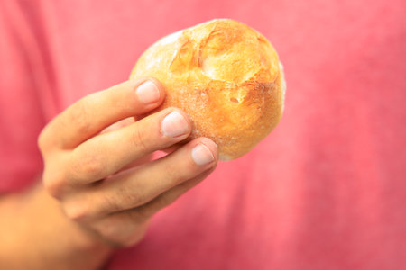 A man's hand holds a round bun, snack and fast food concept. Selective focus on hands with blurred background and copy space for text.の写真素材