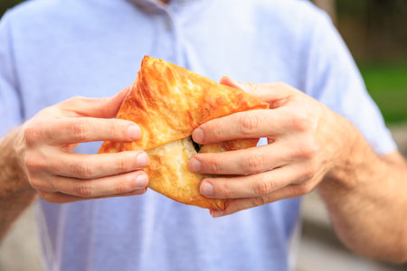 A man's hand holds a puff pastry with cheese, snack and fast food concept. Selective focus on hands with blurred background and copy space for text.の写真素材
