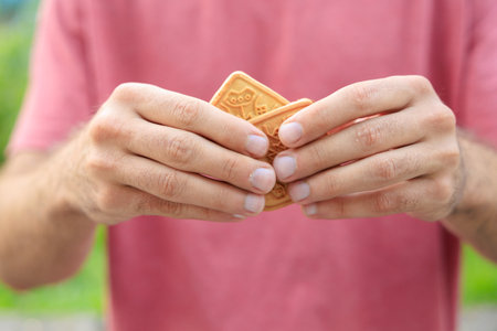 Guy's hand holds cookies, snack and fast food concept. Selective focus on hands with blurred...