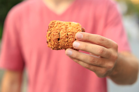 A guy's hand holds a sweet pastry with jam, snack and fast food concept. Selective focus on hands with blurred background and copy space for text.の写真素材