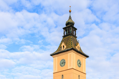 A tall clock tower with a gold roof and a weather vane on top. The sky is mostly clear with a few...