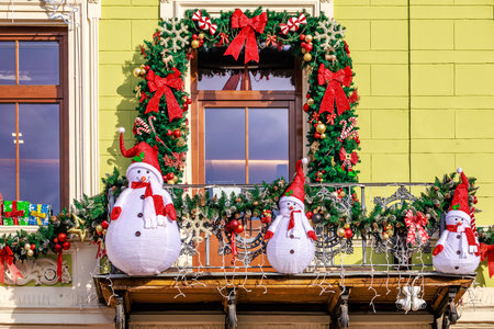 Three snowmen are decorating a balcony with Christmas decorations. The snowmen are wearing hats and are surrounded by a wreath of greeneryの写真素材