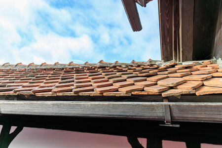Rustic clay tile roof against blue sky on traditional wooden structure.