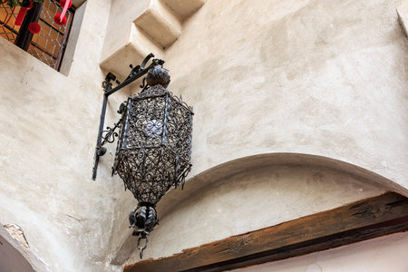 Intricate metal lantern hanging on rustic stone wall of historic european building.