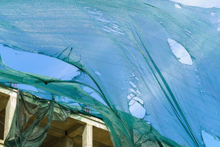 Protective mesh on scaffolding torn by wind. Background with selective focus and copy space for...