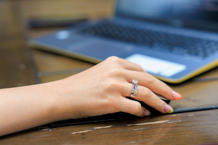 Female hand with elegant ring using laptop on wooden desk.の写真素材