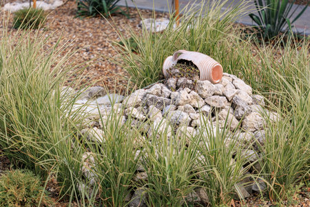 Broken clay pot amidst rock garden with lush green grass.
