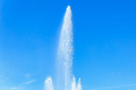 Tall fountain jet against clear blue sky.